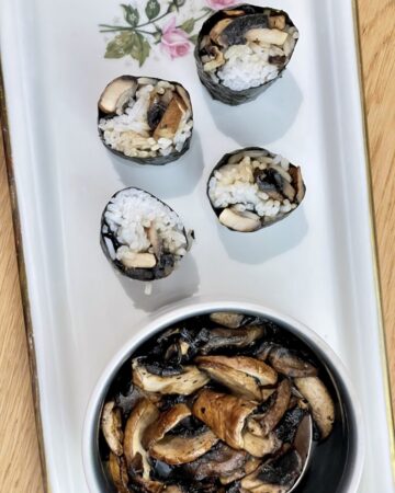 White platter with cream bowl of mushrooms next to four pieces of mushroom sushi