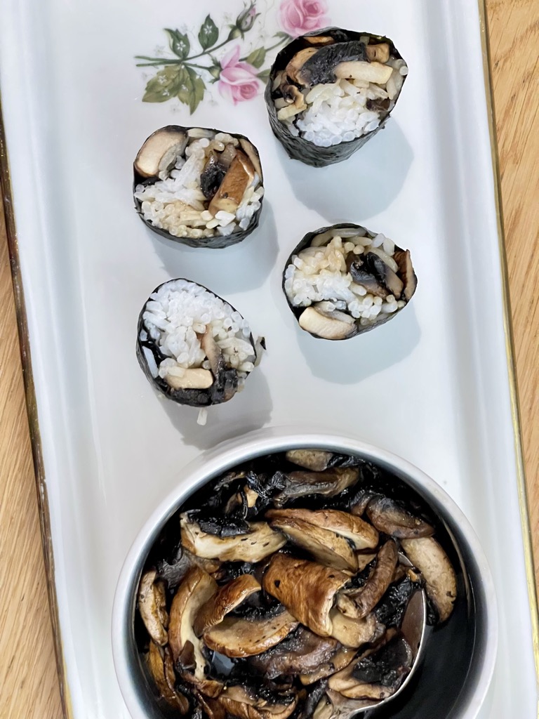 White platter with cream bowl of mushrooms next to four pieces of mushroom sushi