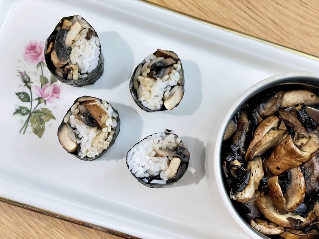 White floral platter with mushroom sushi next to bowl of mushrooms