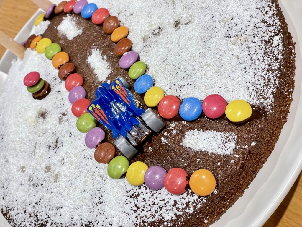 cake decorated as road design made from smarties and powdered sugar with blue hot wheels car driving on road