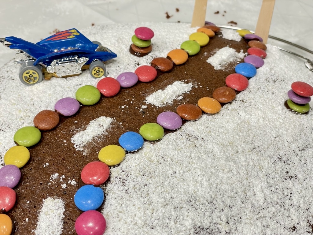 Cake with road design from powdered sugar and smarties and hot wheels car