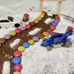 cake decorated as road design made from smarties and powdered sugar with two hot wheels cars parked on either side of the road