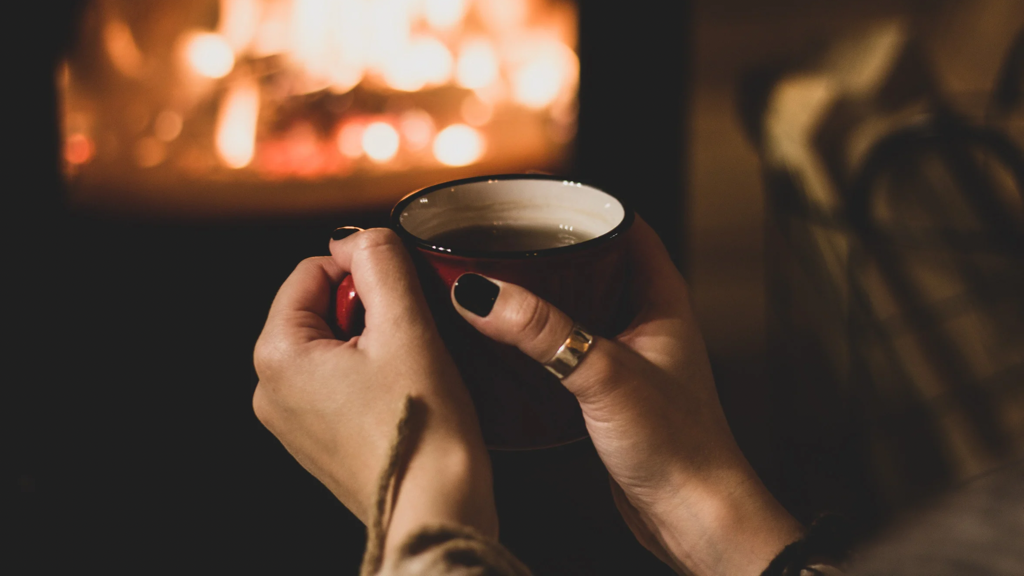 Woman's hands wrapped around red mug in front of fire