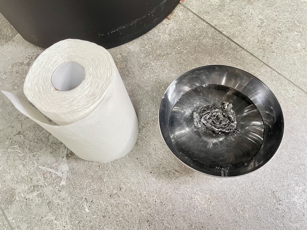 Roll of paper towel next to silver bowl filled with water and steel wool scourer