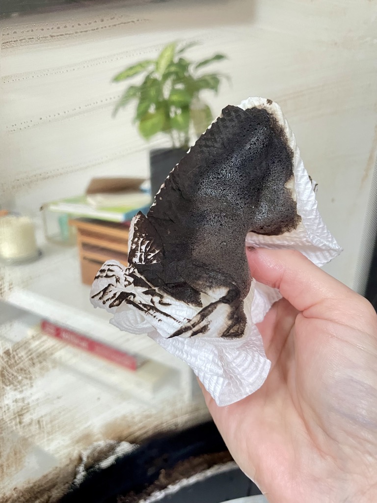 Hand holding blackened paper towel in front of glass panel