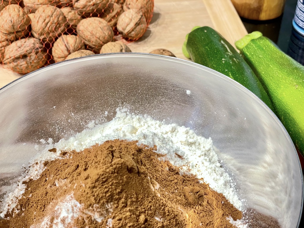 Silver bowl with flour and cinnamon next to net of walnuts and zucchini