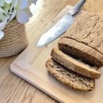 Sourdough discard zucchini bread, sliced on wooden board with knife and flowers