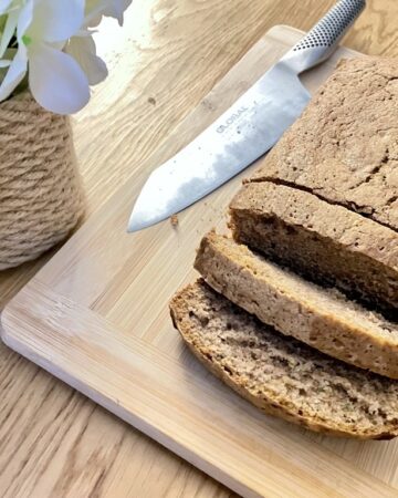 Sourdough discard zucchini bread, sliced on wooden board with knife and flowers