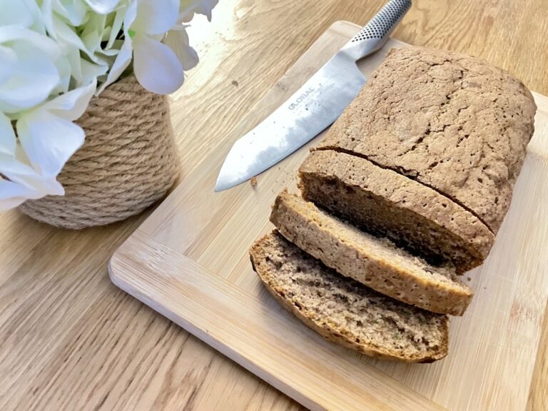 Sourdough discard zucchini bread, sliced on wooden board with knife and flowers