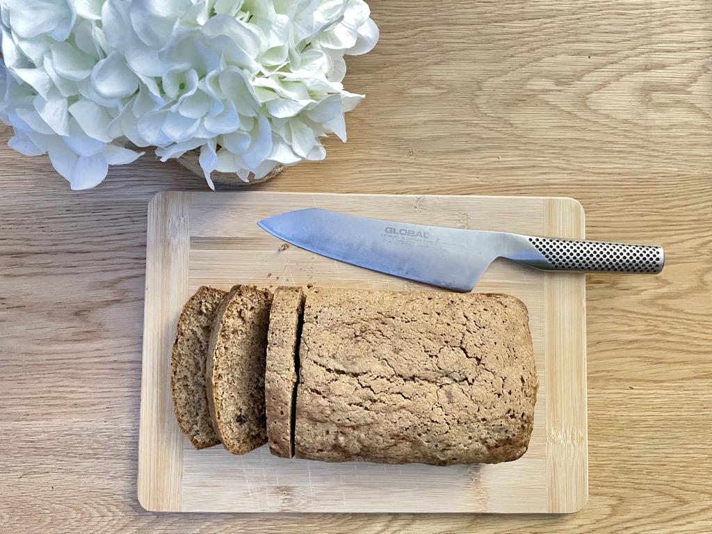 Sourdough discard zucchini bread on wooden board on table, next to flowers and kitchen knife