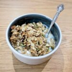 Close up shot of bowl on wooden table filled with yoghurt and granola and silver spoon