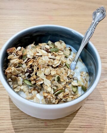 Close up shot of bowl on wooden table filled with yoghurt and granola and silver spoon