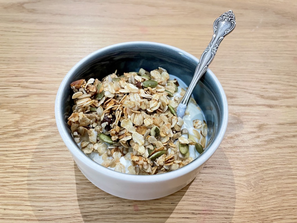 Close up shot of bowl on wooden table filled with yoghurt and granola and silver spoon