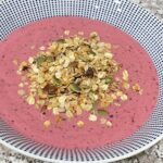 Bowl filled with pink smoothie and topped with granola