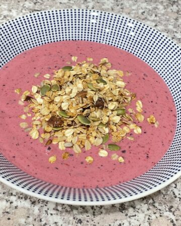 Bowl filled with pink smoothie and topped with granola