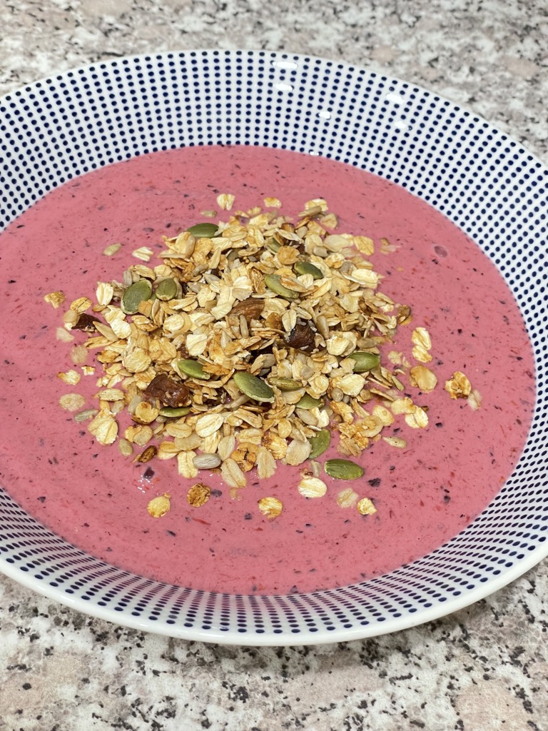 Bowl filled with pink smoothie and topped with granola