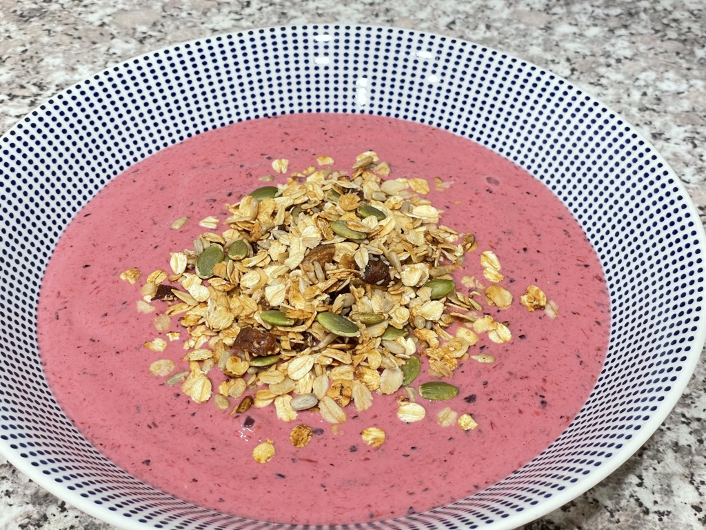 White bowl with blue dots filled with pink smoothie and granola