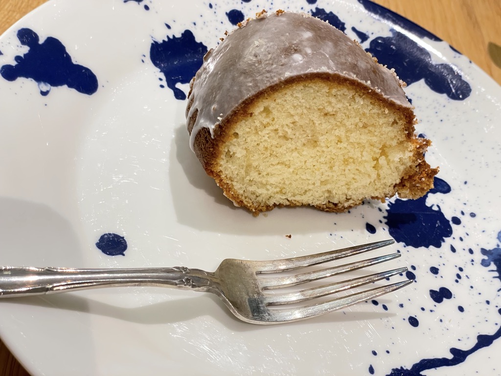 Single slice of rustic homemade lemon drizzle cake on white and blue plate with silver fork