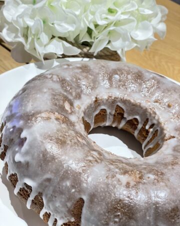 Rustic homemade lemon drizzle cake next to white flowers