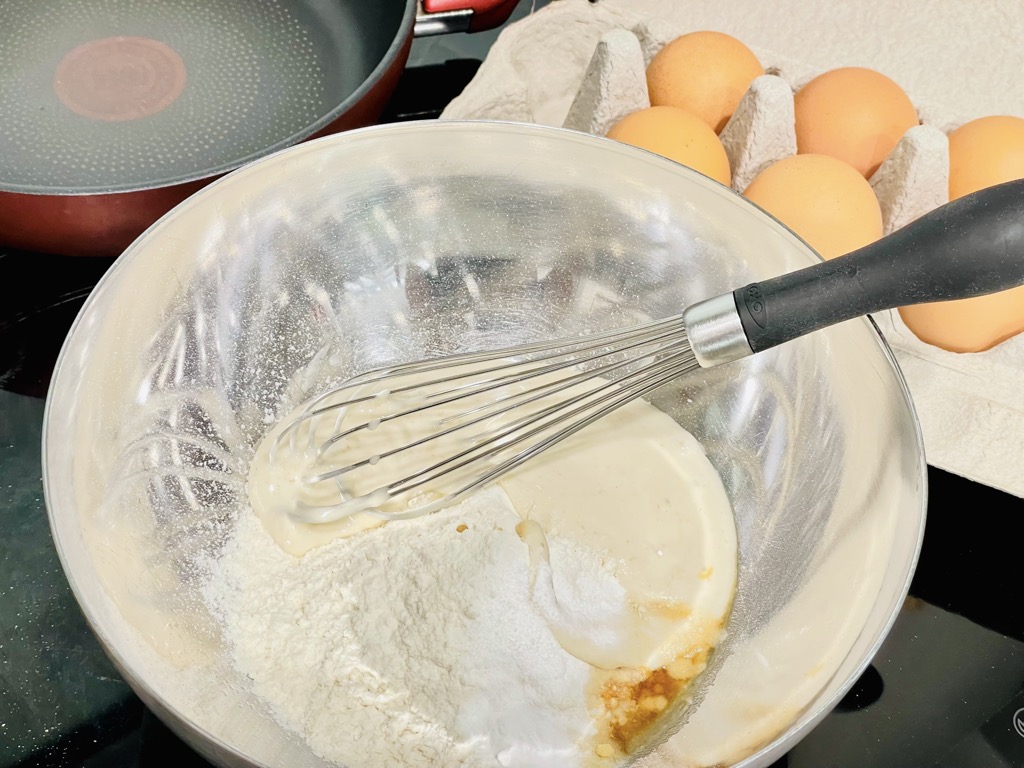 Silver bowl filled with flour and sourdough starter next to carton of eggs and frying pan