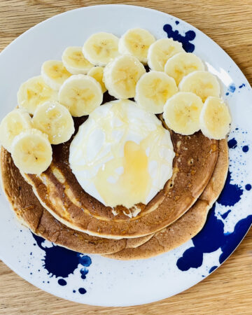 Plate of fluffy sourdough pancakes topped with yoghurt, honey and banana slices