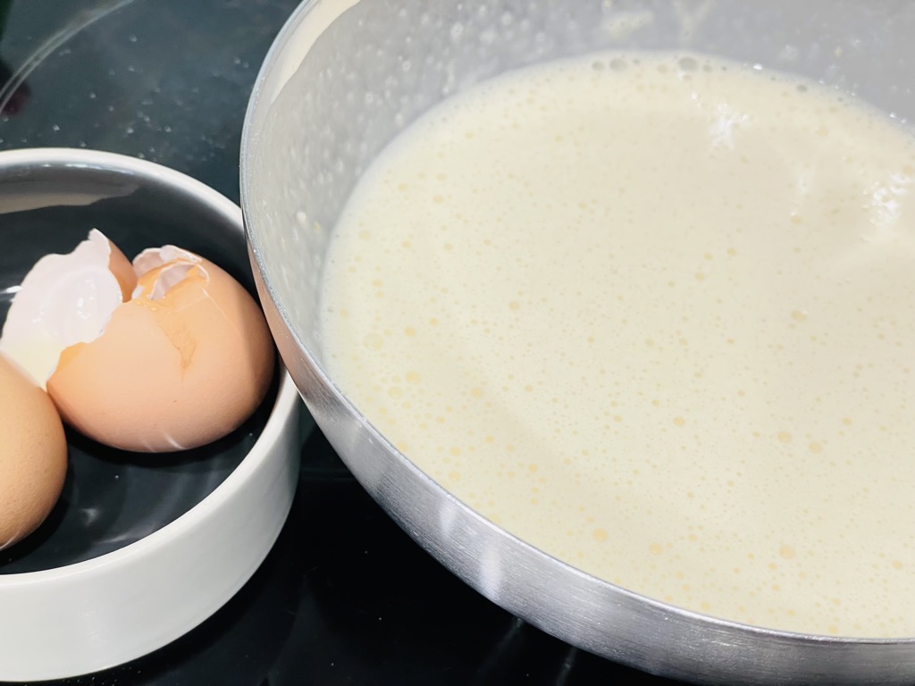 Silver bowl of pancake batter next to bowl of egg shells