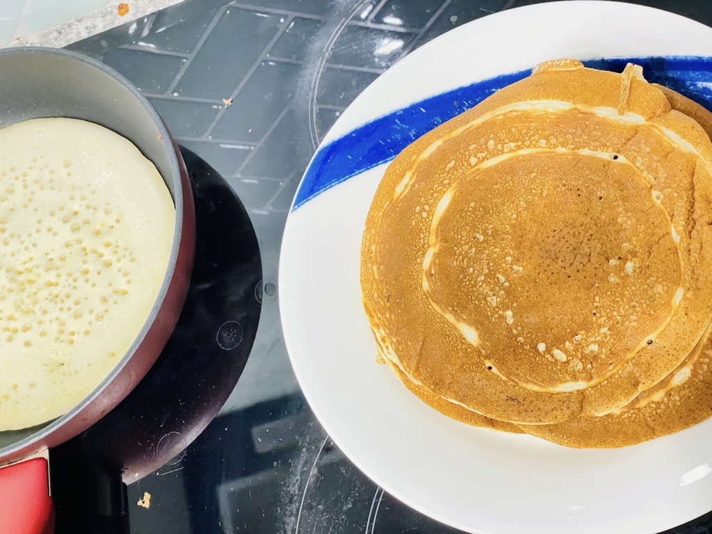 Plate with sourdough pancakes next to red frying pan filled with pancake batter