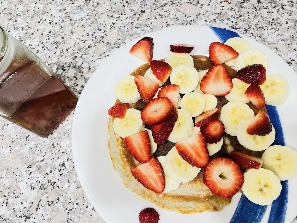 Plate of pancakes with fruit toppings standing next to jar of honey on bench top