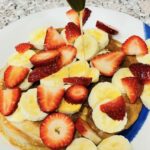 Plate of pancakes with banana and strawberries, drizzled with honey