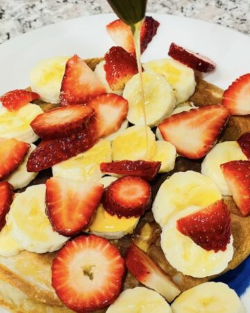 Plate of pancakes with banana and strawberries, drizzled with honey