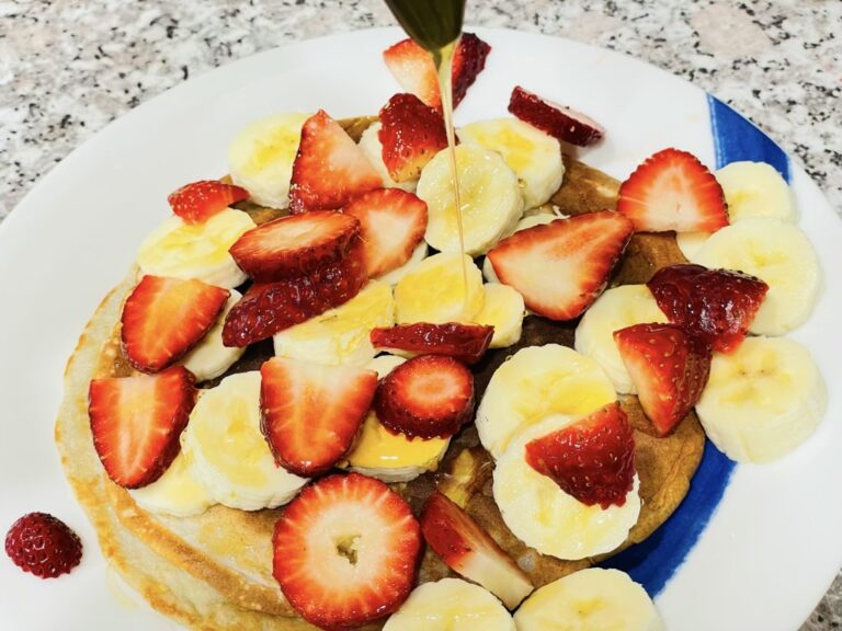 Plate of pancakes with banana and strawberries, drizzled with honey