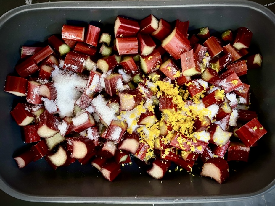 Rhubarb pieces in black bowl, covered in sugar and lemon zest