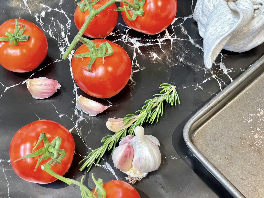 Truss tomatoes, garlic cloves and rosemary sprig on black marble bench