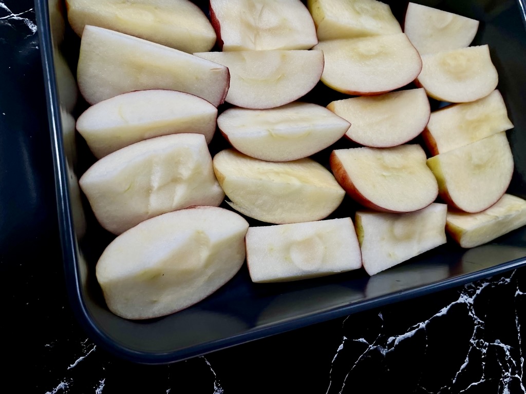 Apple pieces layered in black baking dish on black bench