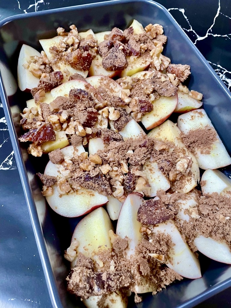 Raw apple pieces topped with date and nut mixture in black baking dish