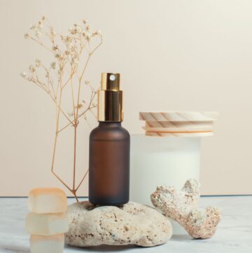 Brown glass spray bottle standing on stone next to glass jar