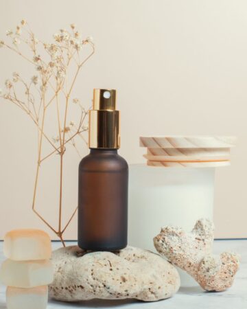 Brown glass spray bottle standing on stone next to glass jar