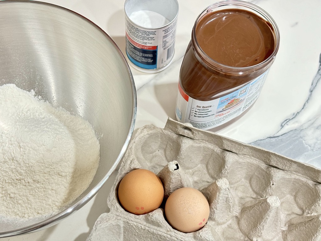 Nutella, flour, eggs and baking powder displayed on kitchen bench