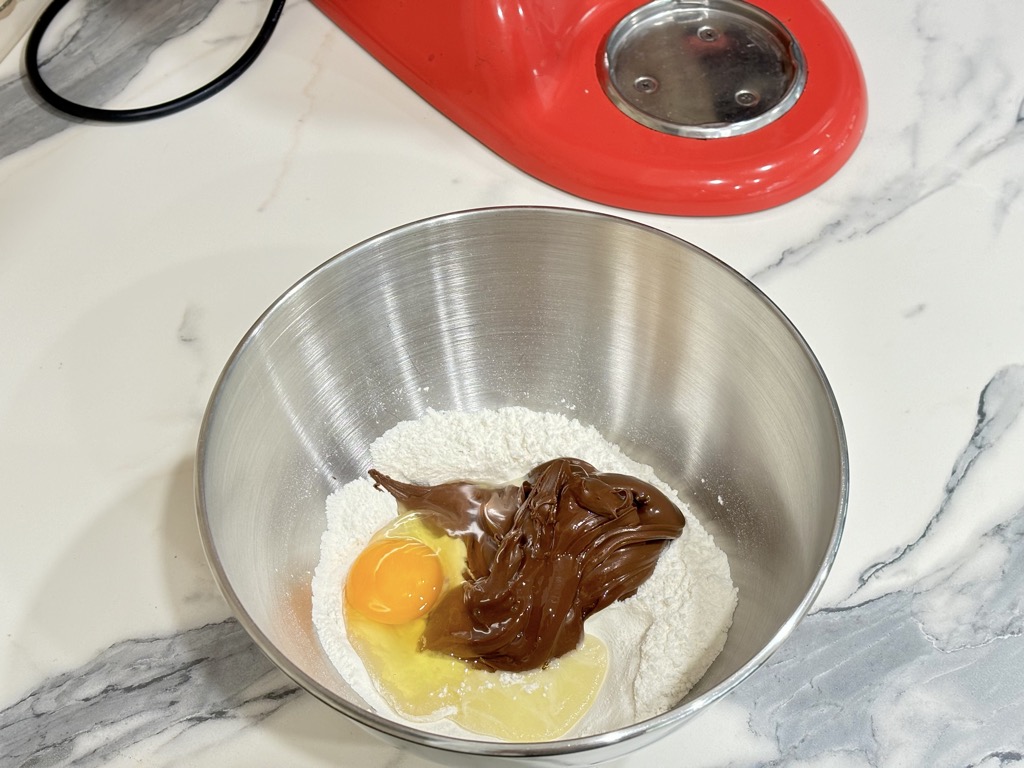 Ingredients for homemade Nutella biscuits in silver mixing bowl next to KitchenAid stand mixer