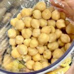 Hand holding clear container filled with cooked chickpeas