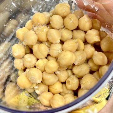 Hand holding clear container filled with cooked chickpeas