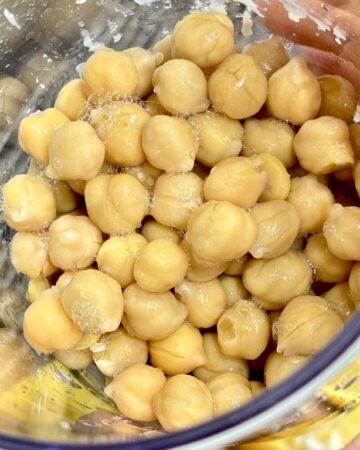 Hand holding clear container filled with cooked chickpeas