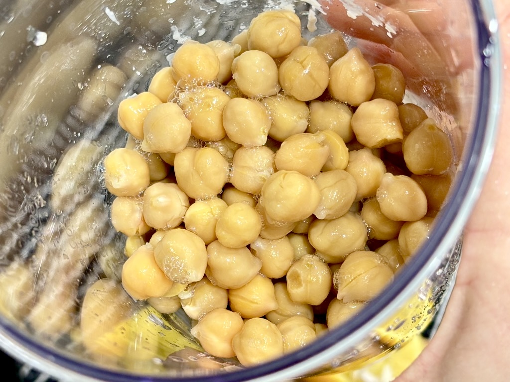 Hand holding clear container filled with cooked chickpeas