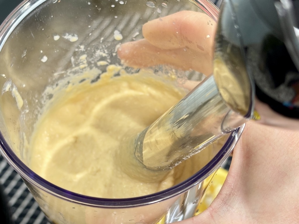 Stick blender submerged in jar of hummus