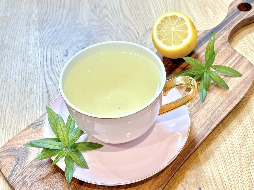 Cup of tea standing on wooden board with lemon and verbena leaves placed on top of it