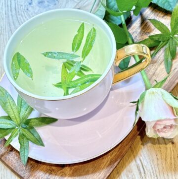 Light pink tea cup with tea leaves and water placed on wooden board with pink rose