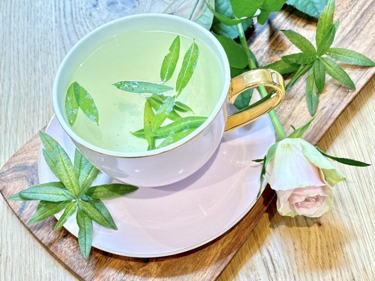 Light pink tea cup with tea leaves and water placed on wooden board with pink rose