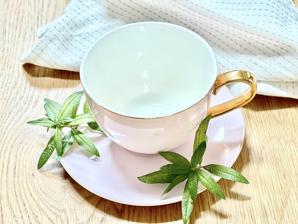 Tea cup with verbena leaves standing in front of white napkin on wooden table