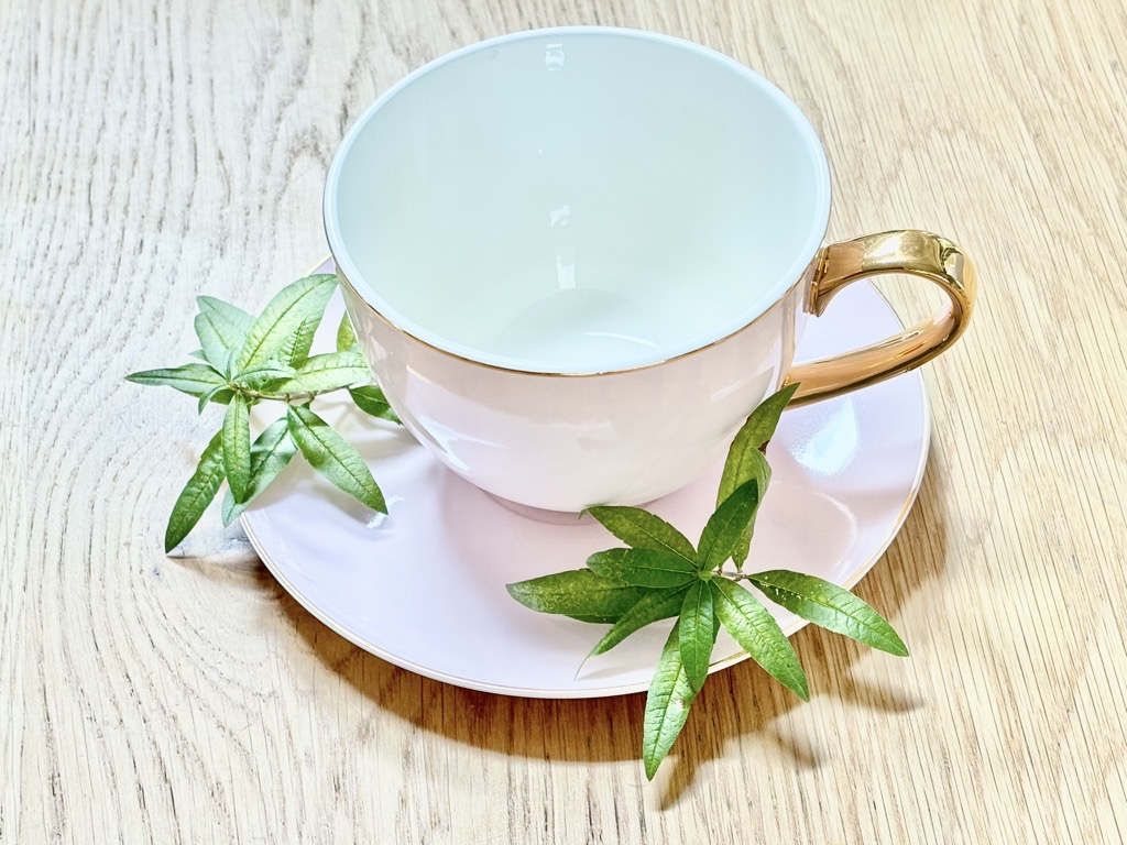 Light pink tea cup on wooden table, with lemon verbena leaves on saucer