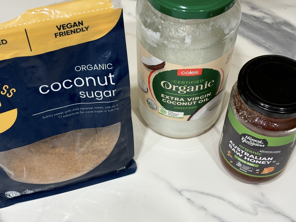 Packets of coconut sugar, coconut oil and raw honey displayed on kitchen bench